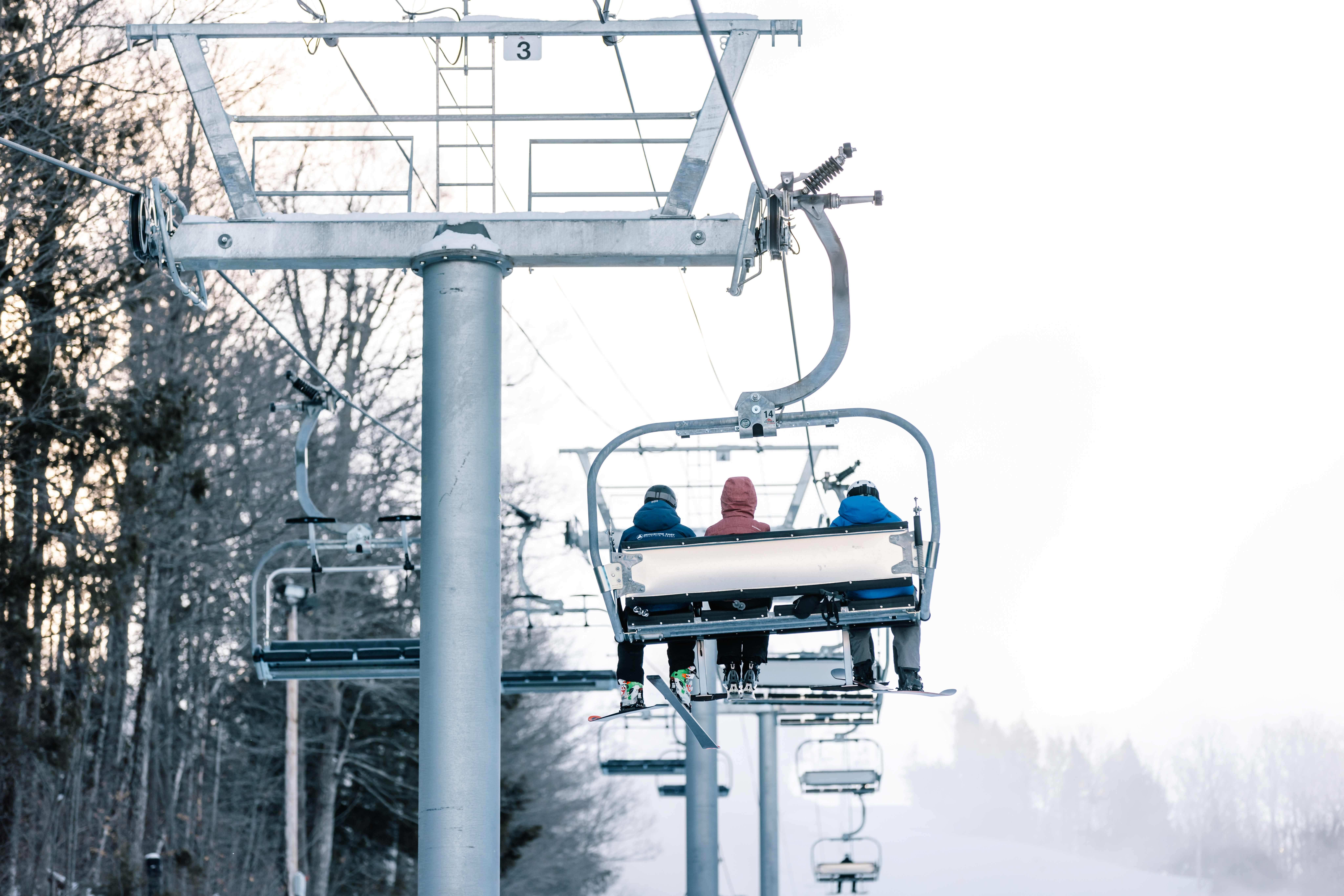 Three Skiers on a chairlift, view from the back.